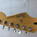 Hlava elektrické kytary z přírodního dřeva s nápisy Fender, STRATOCASTER a MADE IN MEXICO. Je zde uvedeno sériové číslo SERIAL NUMBER MZ6202559. Na h…