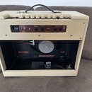 Kytarový kombo zesilovač v krémovém potahu s texturou kůže. Na zadním panelu jsou viditelné nápisy MAINS INPUT, 230V / 50Hz, 115 WATTS, HI POT a EFFE…