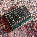 Kytarový efekt v kovovém šasi s černým ovládacím panelem. Na přední straně je tyrkysový nápis BASS MICRO SYNTHESIZER a nad ním značka ELECTRO HARMONI…