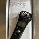 Černý digitální nahrávač značky ZOOM, model H1n Handy Recorder. Zařízení je umístěno v bílém originálním obalu s nápisem Included items. Na horní čás…