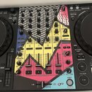 DJ mixážní pult s výrazným, barevným grafickým potiskem v žlutých, růžových a modrých tónech. Na ovládacích prvcích jsou viditelné nápisy SOUND COLOR…
