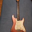 Elektrická kytara s růžovo-měděným lakem a bílým pickguardem. Na hlavě hředu je viditelné logo Fender. Lak na těle vykazuje známky opotřebení, zejmén…