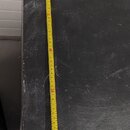 Černý, hranatý reproduktorový box s texturovaným povrchem. Na jeho výšce je přiložen žlutý skladovací metr, který ukazuje hodnotu cca 61 cm. Povrch j…