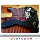 Černá elektrická kytara s červeným mramorovaným pickguardem a světlým hnedým hmatníkem. Nástroj má tři snímače typu single-coil, třetí knoflík a pěti…