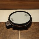 Elektronický buben v černé barvě s bílou membránou. Na povrchu jsou viditelné nápisy Roland a logo značky REMO. Nástroj má chromovaný obruč a je vyba…