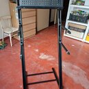 Černý kovový stojan na klávesové nástroje s perforovanou horní deskou. Stojan má nastavitelné výškové mechanismy a dvě boční opěrky pro zajištění nás…