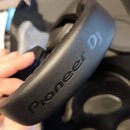 Černé sluchátka s nápisem Pioneer DJ na náhlavním oblouku. Nástroj je umístěn v černém přepravním kufru. Povrch materiálu vypadá hladce a bez viditel…