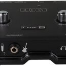 Černý zvukový interface s nápisy UX1 a LINE 6. Na horní straně jsou dva kovové otočné ovladače s popisky MIC GAIN a OUTPUT. V dolní části jsou vstupy…