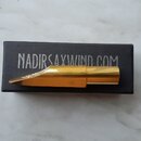 Zlatý kovový mouthpiece na saxofon položený na černé krabičce. Na krabičce je bílý nápis NADIRSAXWIND.COM a na mouthpieceu je vyryté logo TD. Povrch…