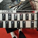 Stříbrný MIDI kontrolér s nápisem FCB1010 MIDI FOOT CONTROLLER. Zařízení má dvě řady černých spínacích pedálů s bílými čísly 1 až 10 a nápisy UP a DO…