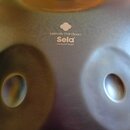 Krytý detail kovového handpanu v tmavě šedé až hnědavé barvě s matným povrchem. Uprostřed je bílý nápis Melody Handpan Sela® a pod ním motto the soul…