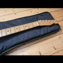 Hrabedlo elektrické kytary s hnedým dřevěným hmatníkem a světlou hlavou. Na hlavě je viditelné logo Fender a nápis Stratocaster. Kytara leží v černém…