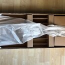 Kytara zabalená v bílém ochranném papíře uvnitř hnědé kartonové krabice s vložkami. Nástroj leží na dřevěné podlaze. Na fotografii nejsou žádné vidit…