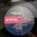 Fotografie detailu středu vinylové desky s etiketou. Na žlutém a modrém pozadí je uveden název kapely a alba CRIMSON GLORY, značka ROADRUNNER RECORDS…