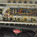 Fotografie zachycuje vnitřek elektronického zařízení, pravděpodobně zesilovače, s viditelným zapojením komponentů na černé desce. Na vnitřní straně š…