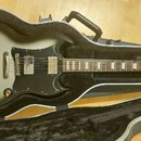Stříbrná elektrická kytara v černém tvrdém kufru. Na hlavě hрифu je bílé logo Epiphone a nápis SG. Kytara má černý pickguard, dva humbuckery a čtyři…