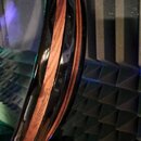 Detailní pohled na hranu kulatého předmětu, pravděpodobně těla nástroje. Je vidět vrstvení černého lakovaného povrchu a hnědého dřeva. Povrch je lesk…