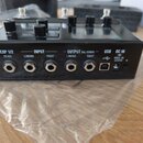 Černý elektronický přístroj s ovládacími knoflíky a displejem. Na zadní straně jsou konektory s nápisy: EXP 1/2 FS 4/5, INPUT L/MONO a RIGHT, OUTPUT…