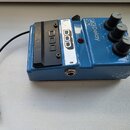 Modrý kytarový efekt s nápisy FXDelay 90 a logem DOD. Na horní straně jsou tři černé otočné oválné knoflíky s popisky DELAY, MIX a REPEAT. Přístroj v…