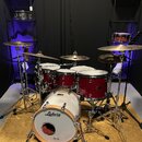 Červená bicí souprava značky Ludwig s bílými bubnovými kožemi. Na předním zrcadle basového bubnu je čitelné logo Ludwig a nápis Classic Maple. Soupra…