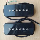 Dvě černé kytarové humbuckery s kovovými ladicími šrouby. Nástroje jsou provedeny v černé barvě s lesklým povrchem, na kterém jsou viditelné drobné š…