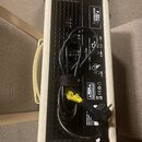 Zadní strana kytarového komba v krémovém potahu s černým zadním panelem. Na panelu jsou viditelné nápisy EXTERNAL SPEAKER IMPEDANCE 8-16 OHMS, RETURN…