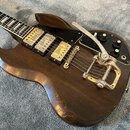 Tmavně hnědá elektrická kytara s tři snímači, na kterých je nápis "Humbucker". Nástroj má instalovaný vibrační systém s páčkou a tři černé ovládací k…