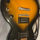 Elektrická kytara s tělem v žlutě-černém gradientním provedení (sunburst). Nástroj má dva humbuckery, dva otočné knoflíky a jeden přepínač. Na těle n…