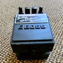 Černý efekt pedál značky BOSS v texturovaném šasi. Na horní části je nalepená bílá nálepka s nápisy OUTPUT, INPUT a Fender '65 Deluxe Reverb Amp. V h…