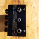 Černý kytarový efekt v kovovém šasi s texturovaným povrchem. Na boku jsou čtyři černé otočné knoflíky a tři konektory: INPUT, 9V DC a OUTPUT. Na čern…