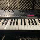 Tmavý syntetizátor s klaviaturaí. Na ovládacím panelu jsou knofíky, posuvníky a tlačítka s nápisy jako FREQUENCY, RESONANCE, MODULATION, FILTER a PRO…