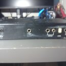 Černý elektronický přístroj s několika konektory na zadní straně. Jsou zde viditelné nápisy EFFECT, REMOTE, OUTPUT, LEVEL a INPUT. V pravém dolním ro…