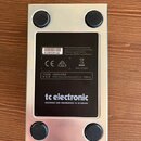 Spodní strana stříbrného efektového pedálu s černým štítkem. Na štítku je uveden nápis tc electronic a text DESIGNED AND ENGINEERED IN DENMARK. Je zd…
