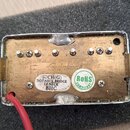 Zadní strana elektrického snímače s kovovým krytem a mosazným základem. Na zadní straně jsou dvě nálepky s nápisy „57CH (G) DOTNECK BRIDGE LP NECK BH…