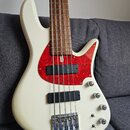 Bílá elektrická basová kytara s červeným vzorovaným pickguardem a hnědým hnedým hmatníkem. Nástroj má dva černé humbuckery a čtyři ovládací knoflíky.…