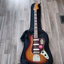 Elektrická kytara s tělem v barvě sunburst a bílým hmatníkem, položená na černém softcasu. Na hlavě je viditelné logo Squier a na těle se nachází čer…