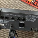 Zadní strana černého mixážního pultu s nápisem YAMAHA POWERED MIXER MODEL EMX2000. Jsou zde vidět výjemy pro SPEAKERS a BRIDGE, napájecí vypínač POWE…