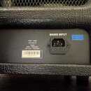 Detail zadní strany černého zesilovače s texturou povrchu. Je zde vidět napájecí konektor s nápisem MAINS INPUT a modrá nálepka HI-POT TESTED. Bílá š…