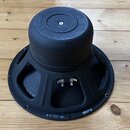 Černý reproduktor s kovovým rámem a magnetem, položený na dřevěném povrchu. Na rámu jsou viditelné nápisy 3 44 06, P 12 100 RP a 2200710. Povrch je m…