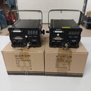 Dvě černé elektronické zařízení s rukojití, umístěná na svých kartonových krabicích. Na přední stranách jsou digitální displeje, konektory s nápisy I…