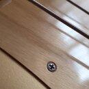 Detailní záběr na hриф kytary s viditelnými strunami. Je zde vidět světlý dřevěný povrch s jedním křížovým šroubem. V horní části je částečně viditel…