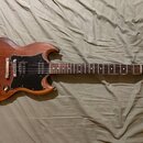 Elektrická kytara s hnědým dřevěným povrchem a černým pickguardem. Na hlavě je viditelné logo Gibson. Kytara má dva humbuckery, čtyři ovládací knoflí…