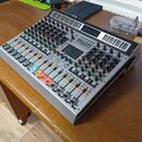 Stříbrný míchací pult s černým horním panelem, vybavený zahlreichen knoflíky a posuvníky. V pravé horní části je viditelný nápis MIXER. Zařízení vyka…