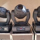 Tři černé moving head reflektory umístěné v transportních kufrech. Na základnách je vidět nápis „Color 575“ a logo „Sino Lighting“. Povrchy zařízení…