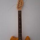 Elektrická kytara s žlutým trupem a hnědým hmatníkem. Na hlavě je viditelný nápis vukomt a kulaté logo. Nástroj má bílý pickguard a je zobrazen s vol…