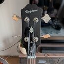 Černá hlava basové kytary s bílým nápisem Epiphone. Na přední straně je umístěn stříbrný ornament ve tvaru stylizovaného hrotu šípu. Nástroj má čtyři…