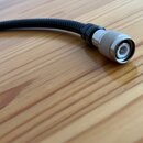 Kabel s černým opleteným povrchem a stříbrným kovovým konektorem. Konektor má vrchovinu s drážkami a v centru je vidět bílý izolátor. Na kabelu ani k…