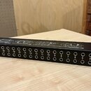 Černý rackový patchbay s řadou 24 zapojovacích jackových konektorů. Nad konektory jsou bílé nápisy s čísly od 1 do 24 a technické schéma zapojení. Na…
