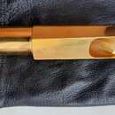 Zlatý kovový mouthpiece pro trubidlo položený na černém koženém pouzdře. Na boku je vyryté malé označení 8 M. Povrch je lesklý s několika drobnými šk…