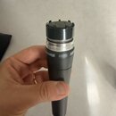 Dynamický mikrofon s černým tělem a stříbrnou mřížkou. Na těle je bílý nápis SMURE SM58 SH. Povrch mikrofonu vykazuje drobné známky opotřebení a zneč…